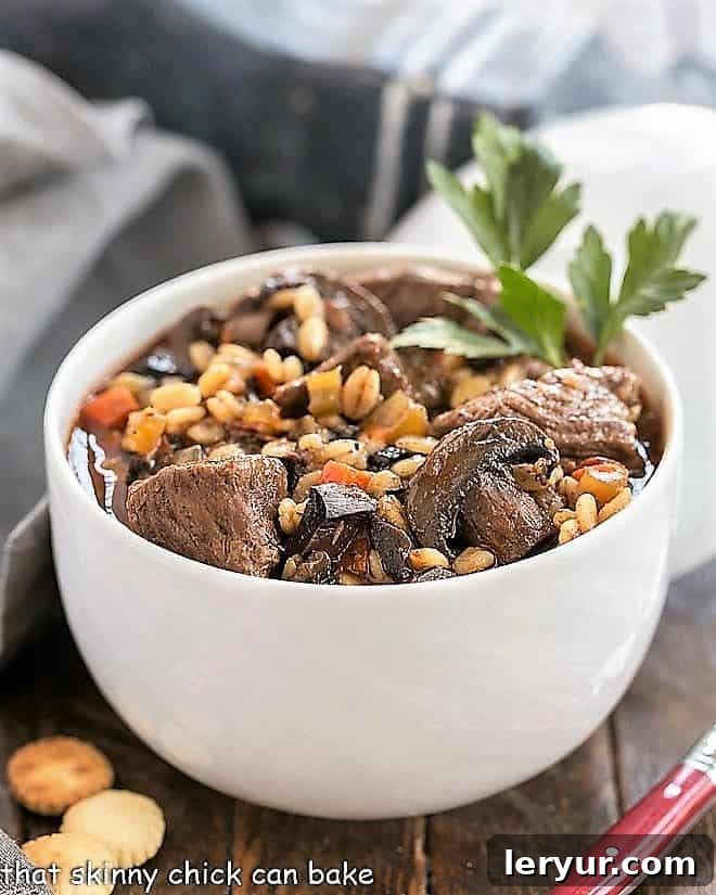 Hearty Beef Mushroom and Barley Soup 3 A close-up shot of Beef Mushroom Soup with Barley in a pristine white bowl, garnished with fresh parsley, highlighting its rich texture and inviting aroma.
