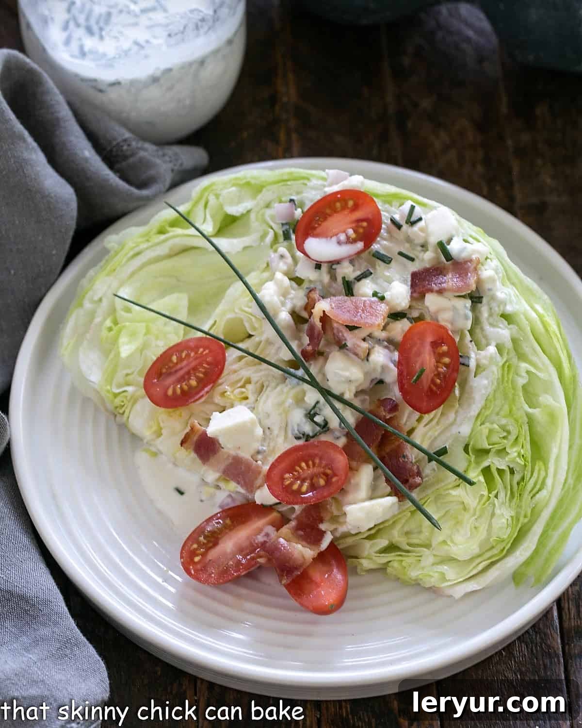 Overhead view of wedge salad on a white plate, showcasing its crisp lettuce, blue cheese dressing, bacon bits, and tomatoes.