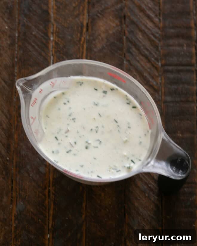 Whisking together ingredients for blue cheese salad dressing in a glass bowl.