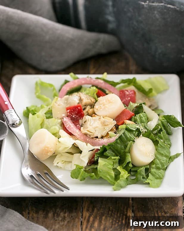 A generous serving of Italian Chopped Salad on a square white plate, accompanied by a fork, ready to be enjoyed.