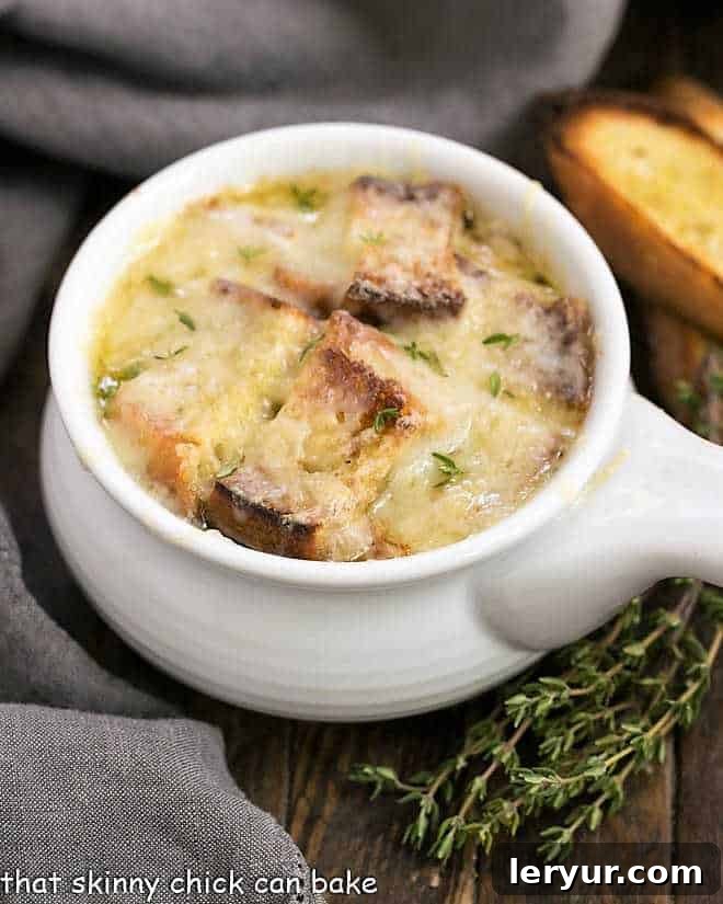 Classic French Onion Soup - A rich onion laden broth flavored with herbs, white wine and cognac and topped with cheesy toast! Classic French Onion Soup in a white ceramic soup bowl, garnished with melted Gruyere cheese and a golden crouton.