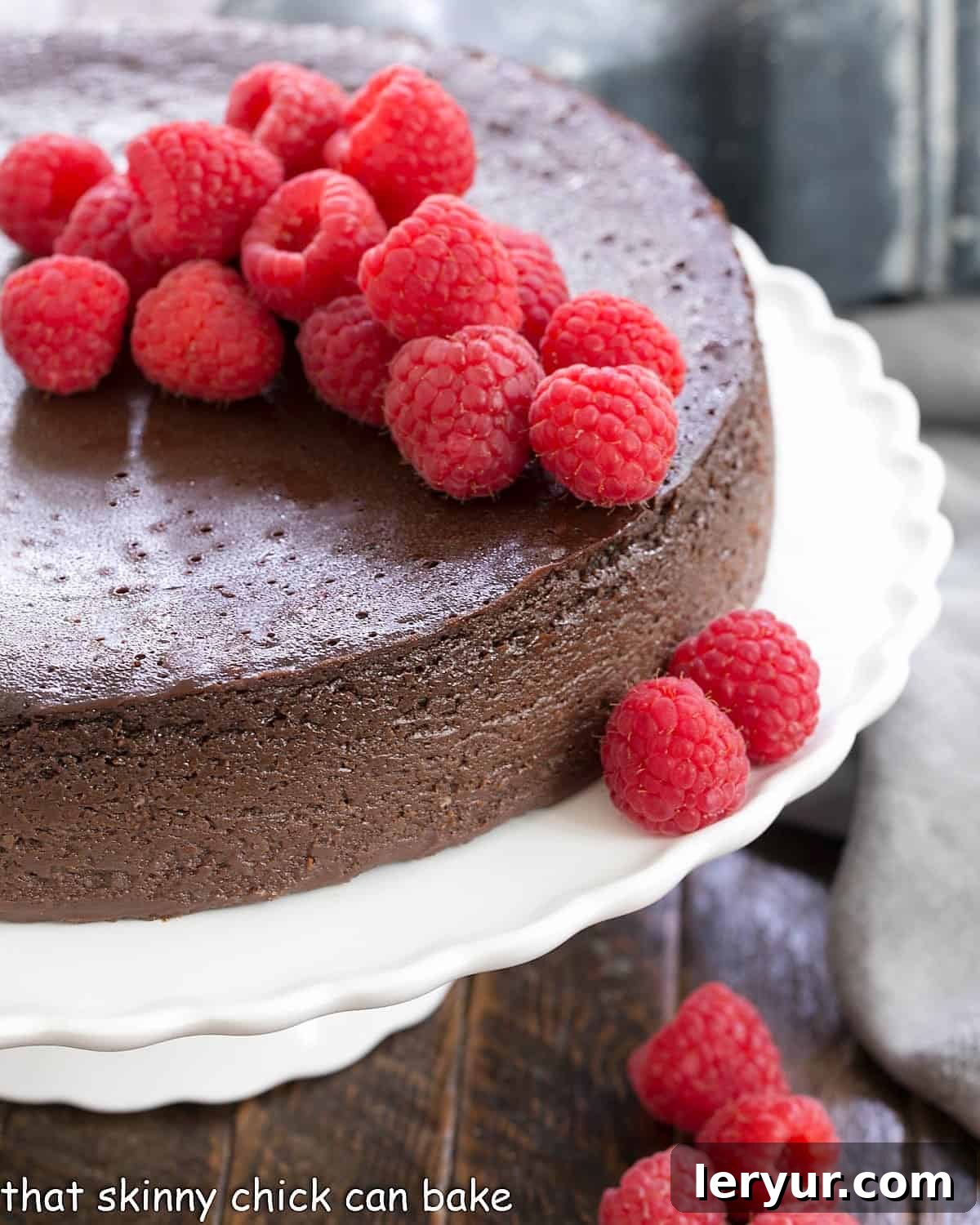 Flourless Chocolate Kahlua Cake - a rich, dense chocolate cake enhanced by coffee liqueur A whole Flourless Chocolate Kahlua Cake on a white cake stand, elegantly topped with fresh raspberries for a vibrant contrast.