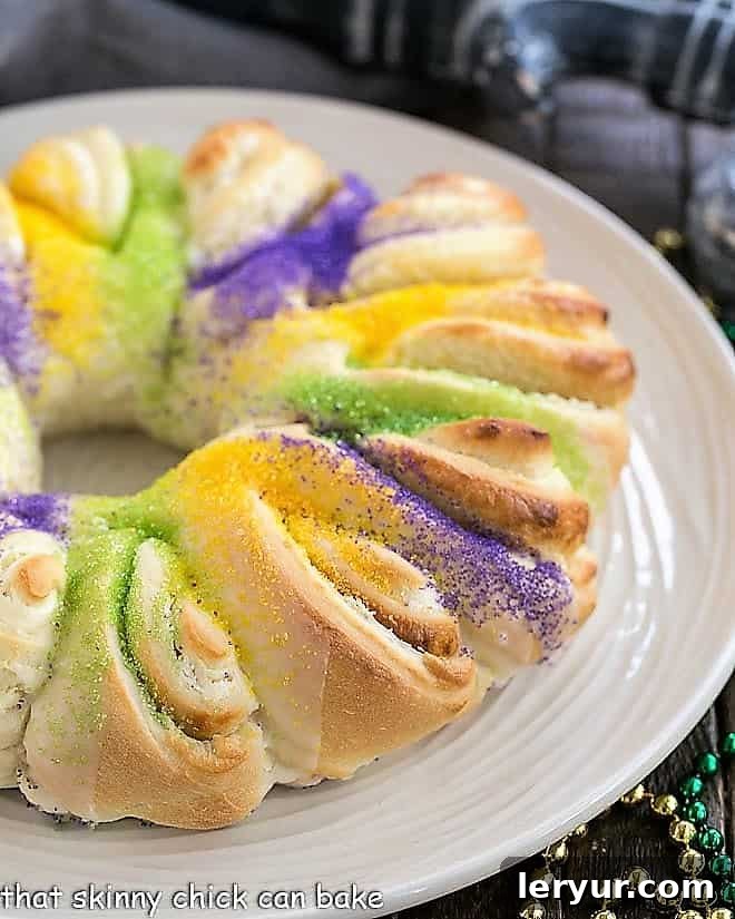 Easy King Cake with cream cheese filling on a white plate, showcasing the vibrant Mardi Gras sugars.