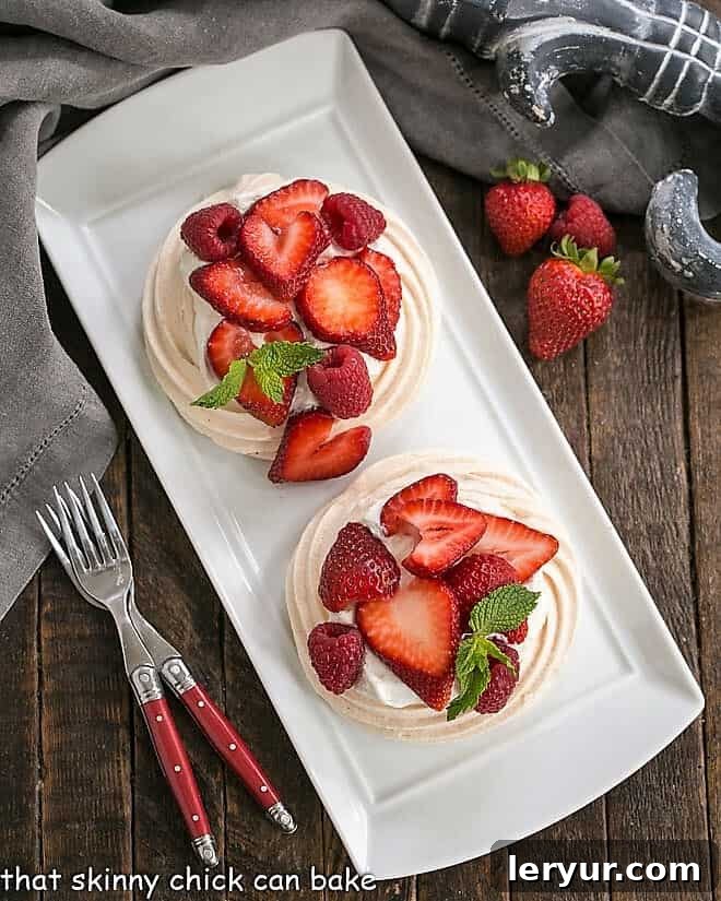Overhead view of two meringue desserts on a white tray with two red handled forks