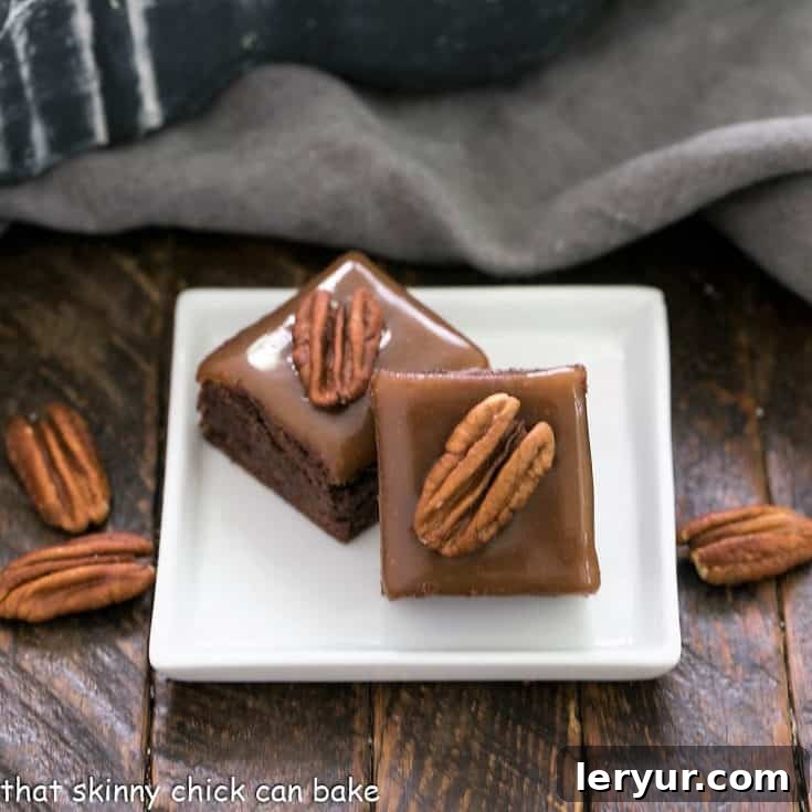 Two turtle brownies on a square white ceramic plate, showcasing the rich layers of chocolate, caramel, and toasted pecans.