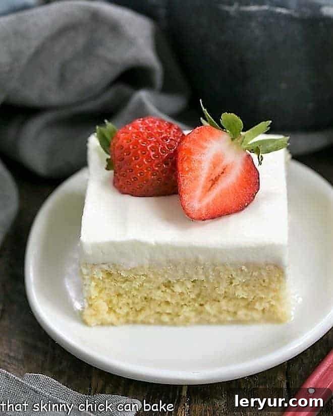Authentic Tres Leches Cake - A Latin American favorite make with 3 milks, a homemade sponge cake and whipped cream frosting! Authentic Tres Leches Cake slice topped with strawberry halves on a white plate.