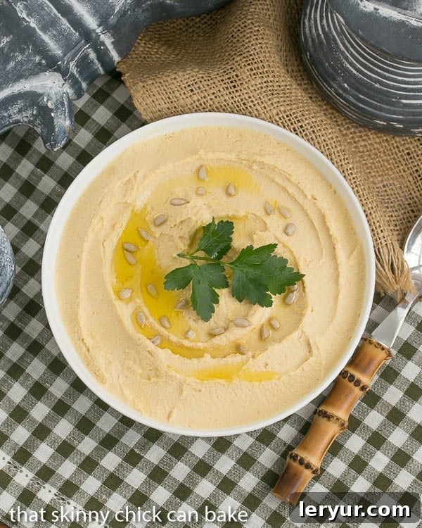 Classic Homemade Hummus: A healthy and flavorful dip infused with fresh lemon and aromatic garlic. Overhead shot of creamy Classic Hummus in a pristine white bowl, elegantly drizzled with olive oil and garnished with a sprinkle of toasted seeds and fresh parsley.