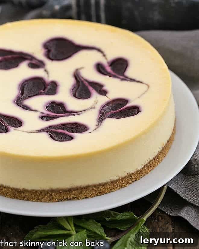 This Blueberry Swirl Cheesecake is one of the most creamy, luscious cheesecakes you'll ever taste! An elegant, uncut Blueberry Swirl Cheesecake presented on a pristine white serving plate.