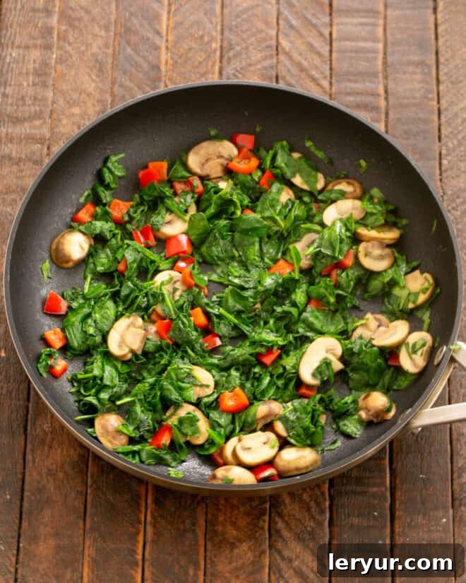 Garden & Woodland Quiche 4 Fresh baby spinach and diced red bell peppers being added to sautéed mushrooms in a skillet, cooking until the spinach wilts.