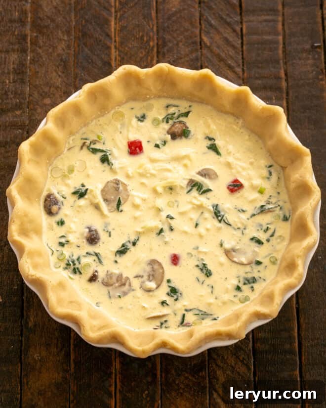 Garden & Woodland Quiche 6 A prepared pastry shell filled with cooked vegetables, shredded cheese, and poured custard, ready for baking.