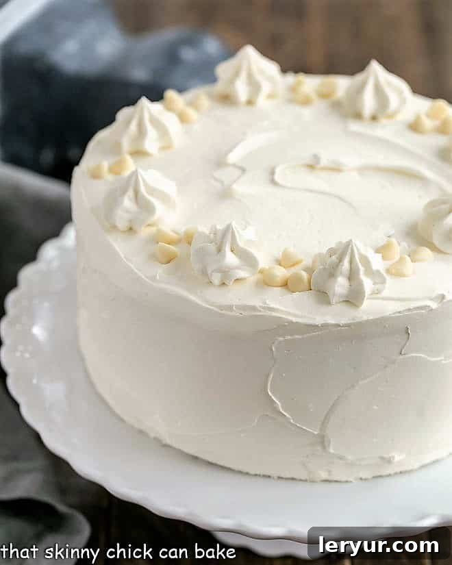 A stunning Classic White Layer Cake adorned with a luxurious White Chocolate Swiss Meringue Buttercream, presented on an elegant white cake stand.