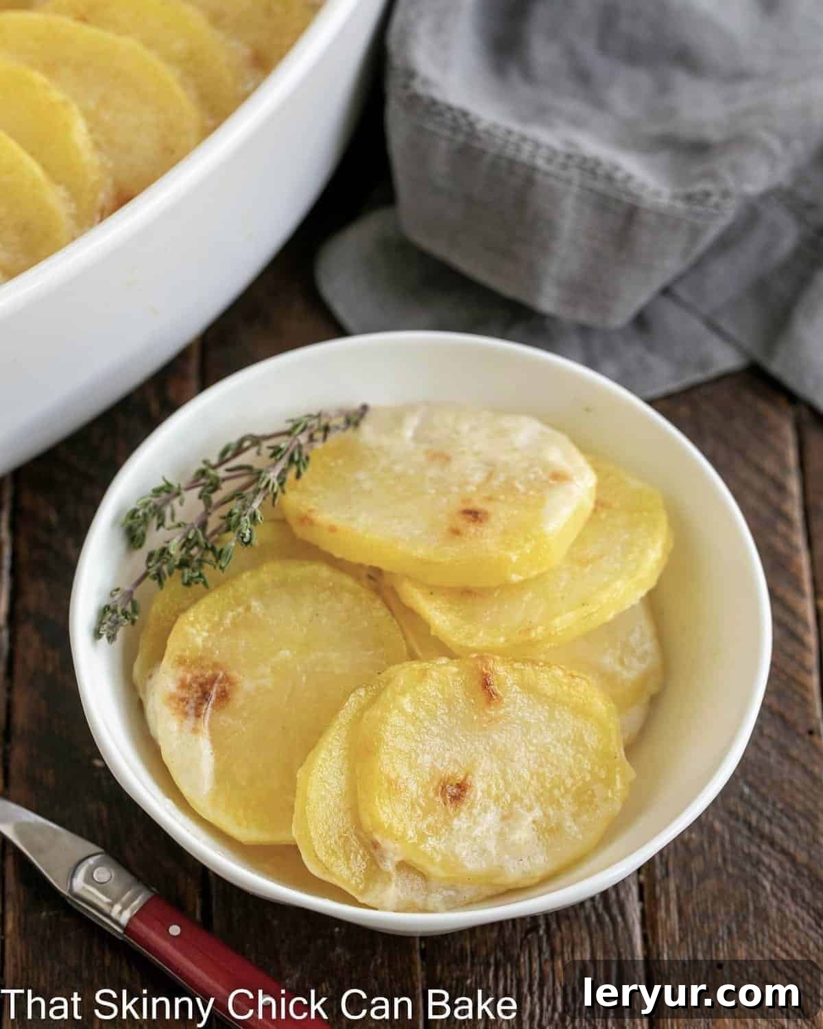 The Best Scalloped Potatoes - Tender, cheesy and perfect every time! Close view of a small bowl of golden brown scalloped potatoes next to the casserole dish, showing the creamy texture and melted cheese.