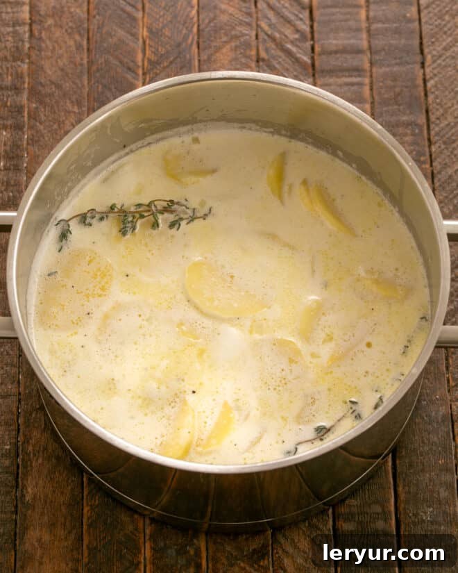 The Only Scalloped Potatoes You'll Ever Need 4 Sliced potatoes simmering in a creamy sauce with herbs in a pot.