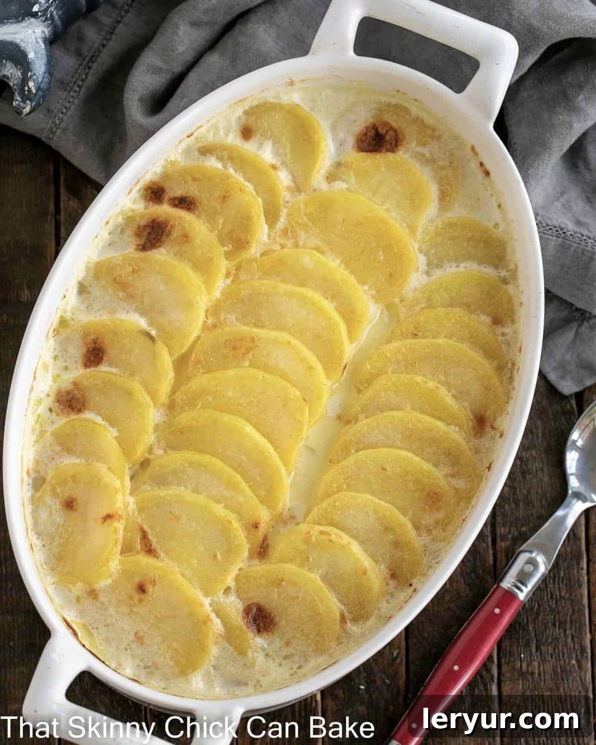 The Best Scalloped Potatoes - Tender, cheesy and perfect every time! Overhead view of cheesy scalloped potatoes in an oval casserole dish, glistening with melted cheese and creamy sauce.