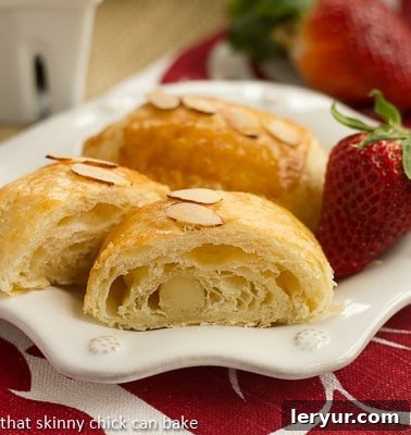 Homemade Almond Croissants on a white decorative plate with a strawberry. Golden brown and perfectly flaky pastries.