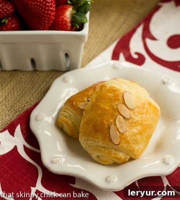 Two almond topped Homemade Almond Croissants on a white ceramic plate. Garnished with sliced almonds.