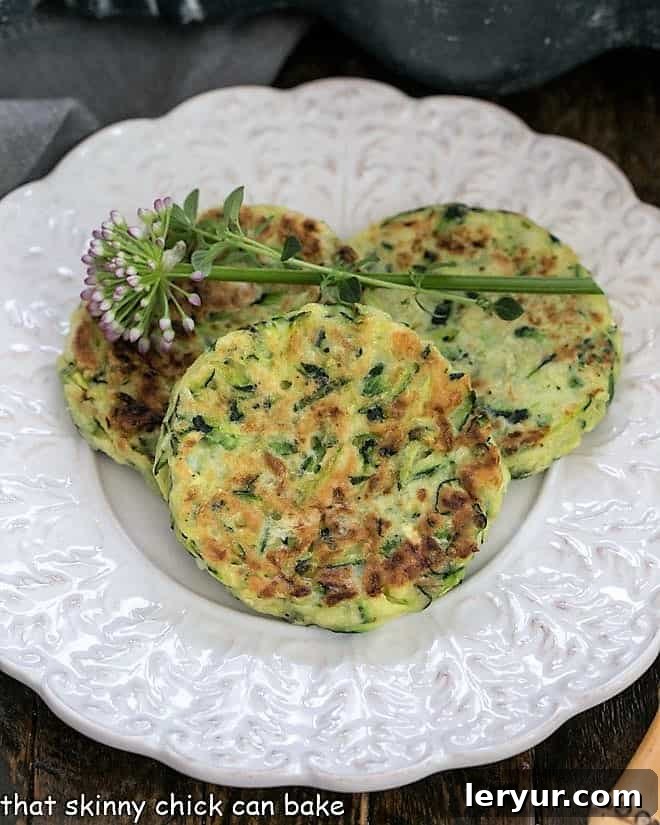 Overhead shot of three perfectly cooked zucchini fritters on a decorative white plate, ready to be enjoyed.