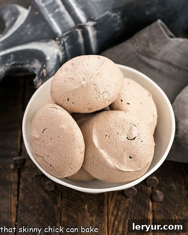 A delicate pile of Chocolate Chip Meringues nestled in a rustic white ceramic bowl, ready for serving. The cookies hint at their crispy texture and delicious chocolate centers.