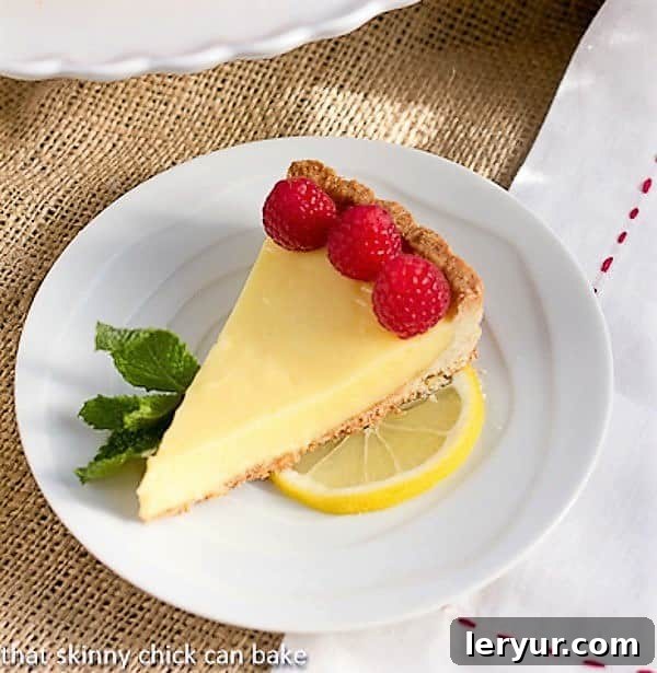 Tarte au Citron AKA French Lemon Tart - An exquisite lemon dessert with a buttery shortbread crust filled with a luscious lemon sabayon A perfect slice of Tarte au Citron, also known as French Lemon Tart, beautifully garnished with fresh, vibrant raspberries, showcasing its creamy filling and golden crust.