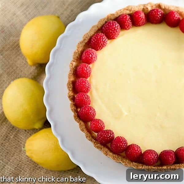 Tarte au Citron - An exquisite lemon dessert with a buttery shortbread crust filled with a luscious lemon sabayon A close-up of a French Lemon Tart, beautifully garnished with fresh raspberries, highlighting the smooth, glossy surface of the lemon filling and the rustic texture of the crust.