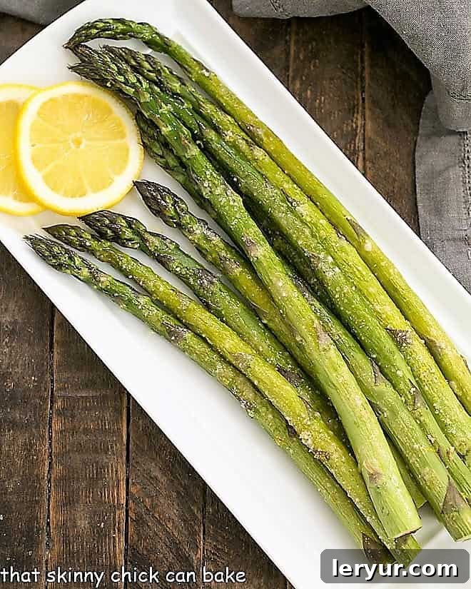Overhead view of Easy Oven Roasted Asparagus on a white tray with lemon slices.