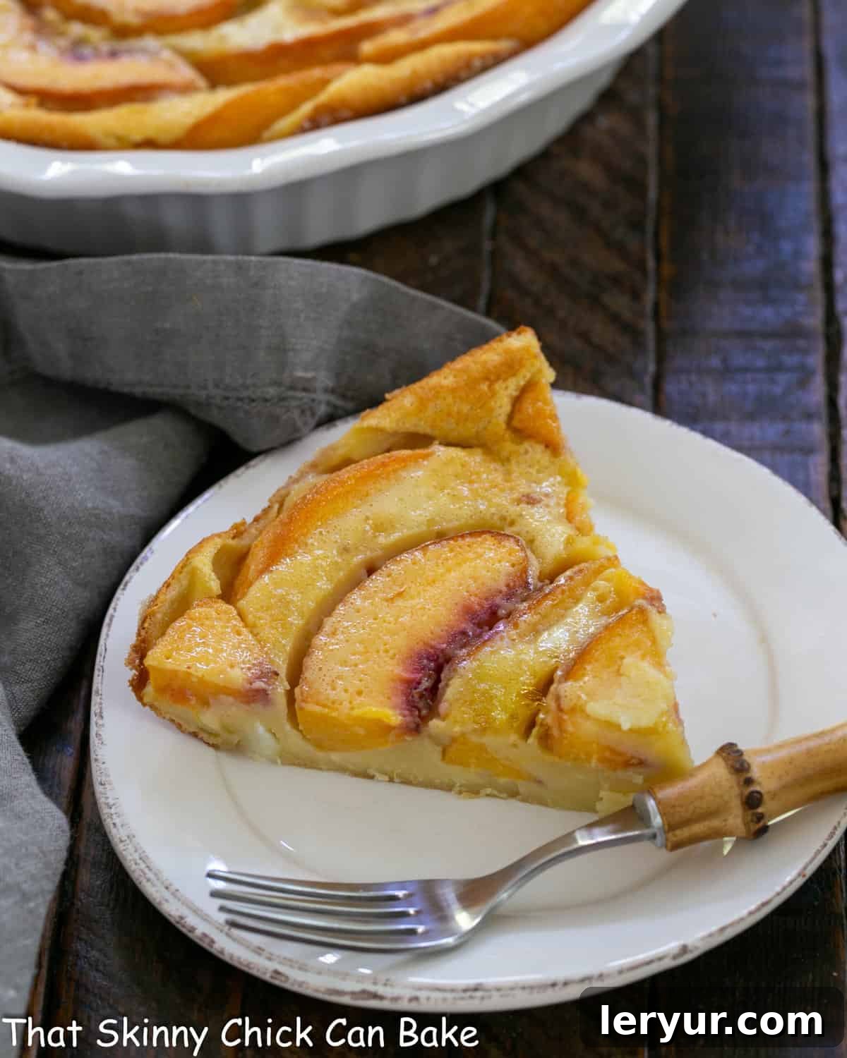 Slice of golden-brown peach clafoutis on a white plate with a delicate bamboo fork, showcasing its custardy texture and vibrant peach slices.