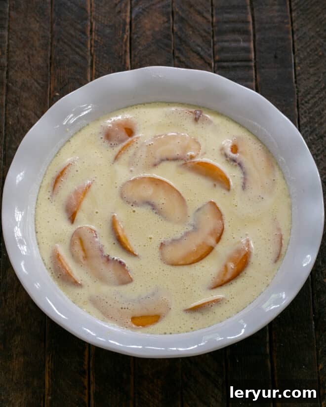 The remaining clafoutis batter is poured over the peaches, completely covering them and filling the dish, ready for baking.