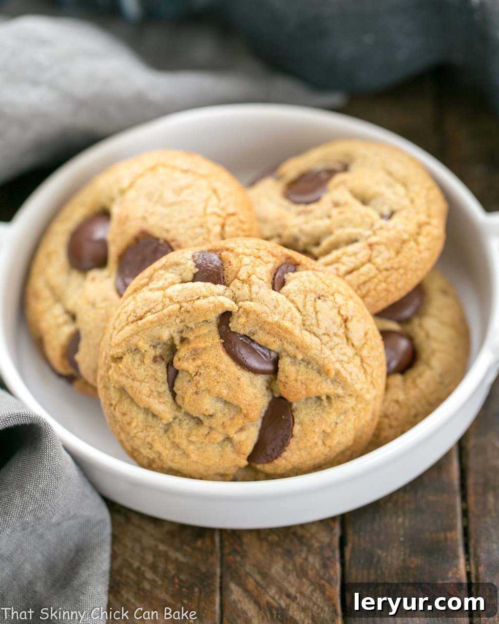Brown Butter Chocolate Chip Cookies - with a boost of deliciousness from nutty brown butter and dark brown sugar! A stack of perfectly baked Brown Butter Chocolate Chip Cookies in a white ceramic dish, showcasing their golden-brown edges and molten chocolate centers. The rich, inviting texture hints at their irresistible flavor.