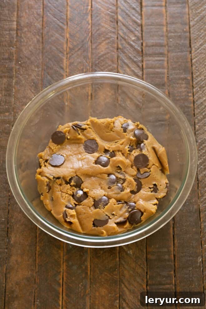 Divine Brown Butter Chocolate Chip Cookies 7 Semi-sweet chocolate discs or chunks being folded into the prepared cookie dough in a mixing bowl, ensuring even distribution.