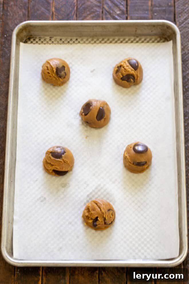 Divine Brown Butter Chocolate Chip Cookies 8 Scooped balls of brown butter chocolate chip cookie dough neatly arranged on a parchment-lined baking sheet, spaced adequately for baking.