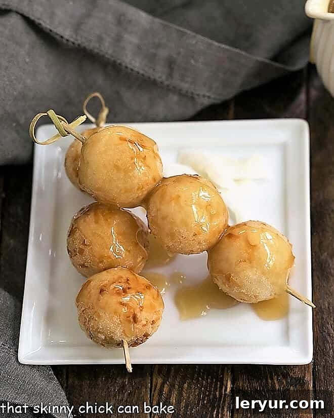 Carioca or Fried Sticky Rice Balls served on wooden skewers on a square white plate, with caramel drizzle