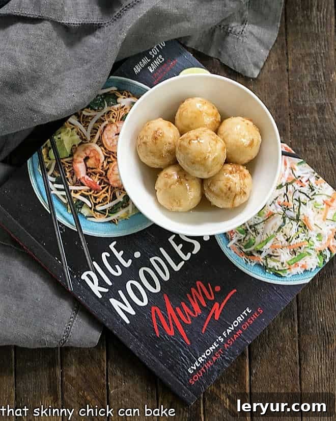 Carioca or Fried Sticky Rice Balls in a white ceramic bowl on top of a cookbook, with a spoon nearby
