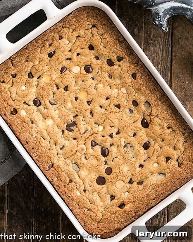 An inviting overhead view of a batch of perfectly baked chocolate chip cookie bars, cooling in a pristine white ceramic baking pan, showcasing their golden-brown tops and rich chocolate pockets.