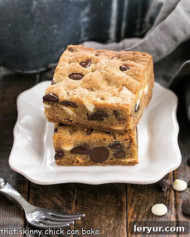 A charming image of two perfectly stacked chocolate chip bars resting on a delicate white dessert plate, accompanied by a small, elegant fork.