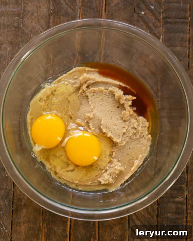 Adding two room-temperature eggs and a generous amount of vanilla extract to the creamed butter and sugar mixture, ready for mixing.