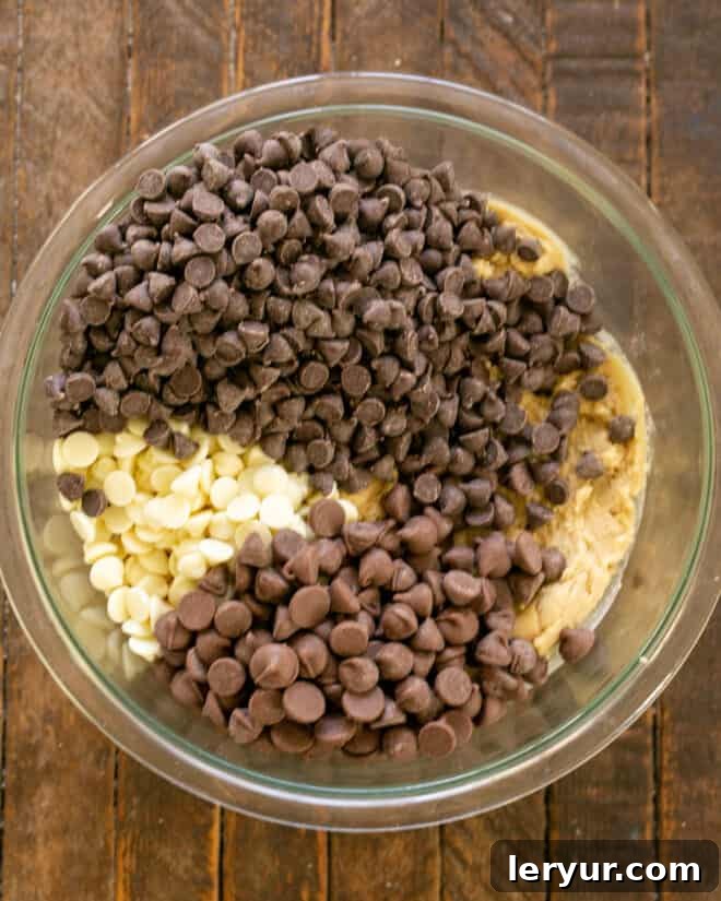 A close-up view of a bowl of cookie dough, with a generous portion of semisweet chocolate chips freshly added, ready to be folded in.