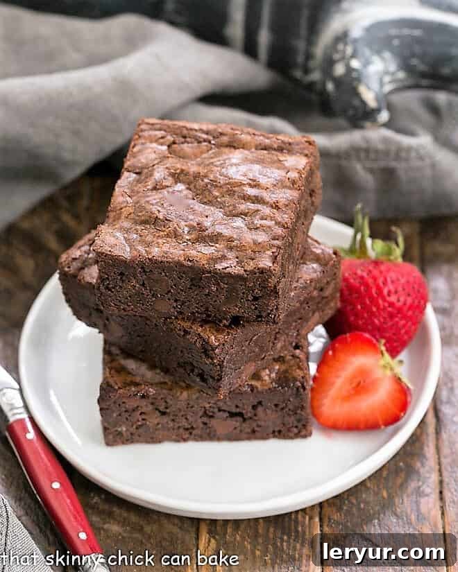 A stack of 3 homemade sheet pan brownies on a small white plate, showcasing their rich, fudgy texture.