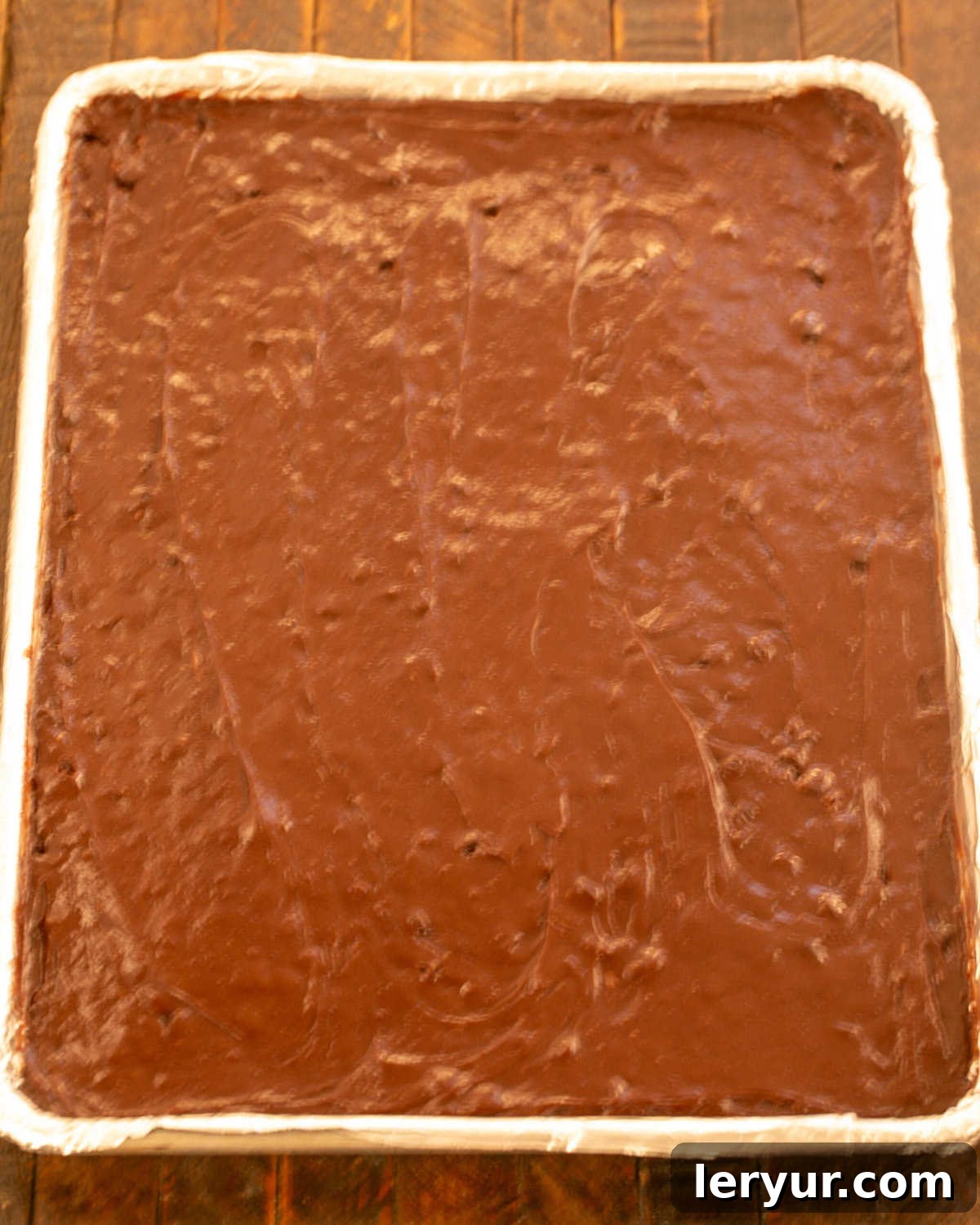 Step 9: Spreading the brownie batter evenly onto the prepared baking sheet with an offset spatula.