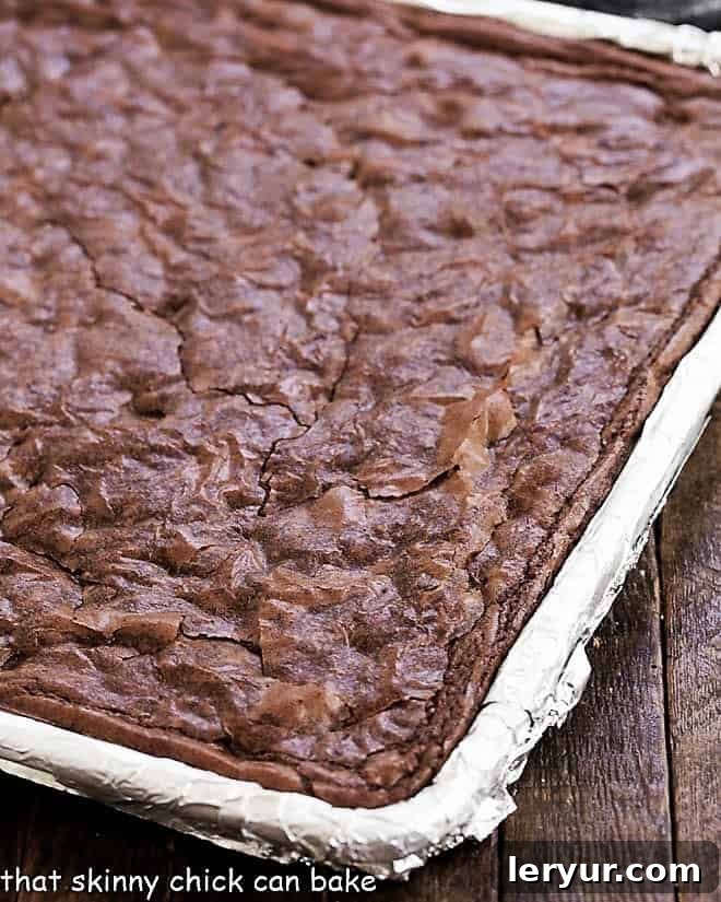Fudgy Sheet Pan Brownies cooling in a baking sheet, impeccably lined with non-stick foil for easy handling.
