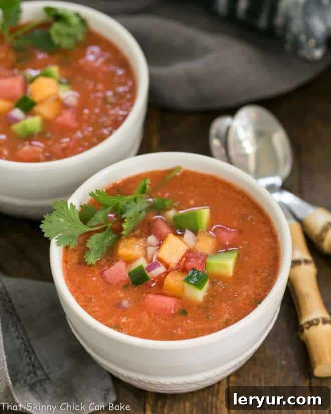 Wazpacho AKA watermelon gazpacho - A cold refreshing summer soup with tomatoes and watermelon! Wazpacho AKA watermelon gazpacho in two white bowls with bamboo handled spoons.