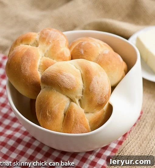 Moomies Buns are easy to make and so tender and delicious! Bakery style rolls you can make at home! A basket of freshly baked Moomie's Buns, golden and tender, resting in a white bowl on a charming red checked napkin.