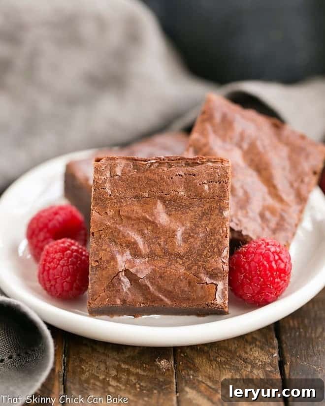 Best Fudgy Brownies - an extra step makes these dreamy and irresistible! Best Fudgy Brownies on a round dessert plate with raspberries to garnish.