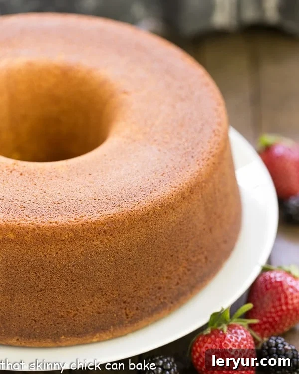 A beautifully golden-brown Whipping Cream Pound Cake resting on a elegant white cake plate, ready to be enjoyed.
