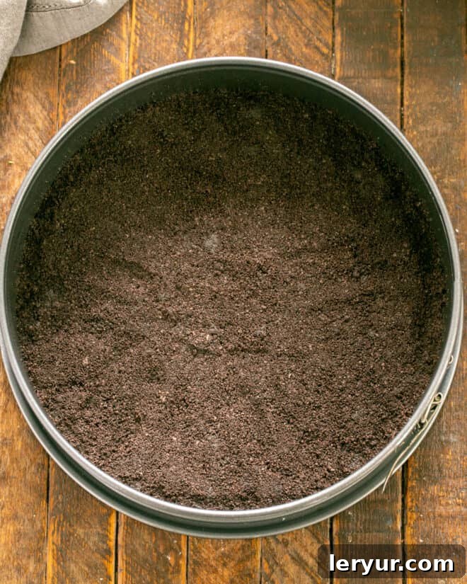 Emerald Oasis Oreo Dream 4 Step-by-step image showing cookie crumbs being pressed into a springform pan to form the crust.