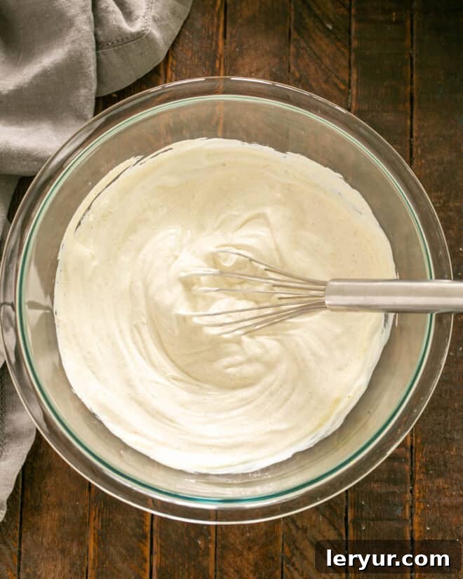 Whisking mayonnaise and sour cream together in a bowl.