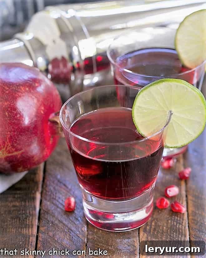Two Pomegranate Cosmopolitan Cocktails in high ball glasses, garnished with lime.
