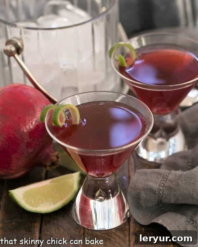 Two Pomegranate Cosmopolitan Cocktails in martini glasses with lime twists and festive decor.