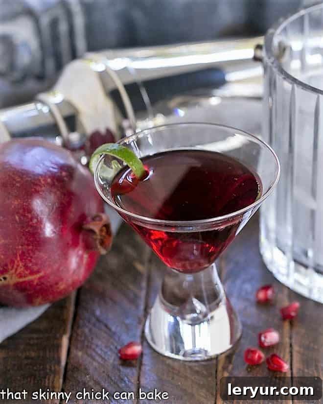 A Pomegranate Cosmopolitan Cocktail in a martini glass with a lime twist, ready for serving.