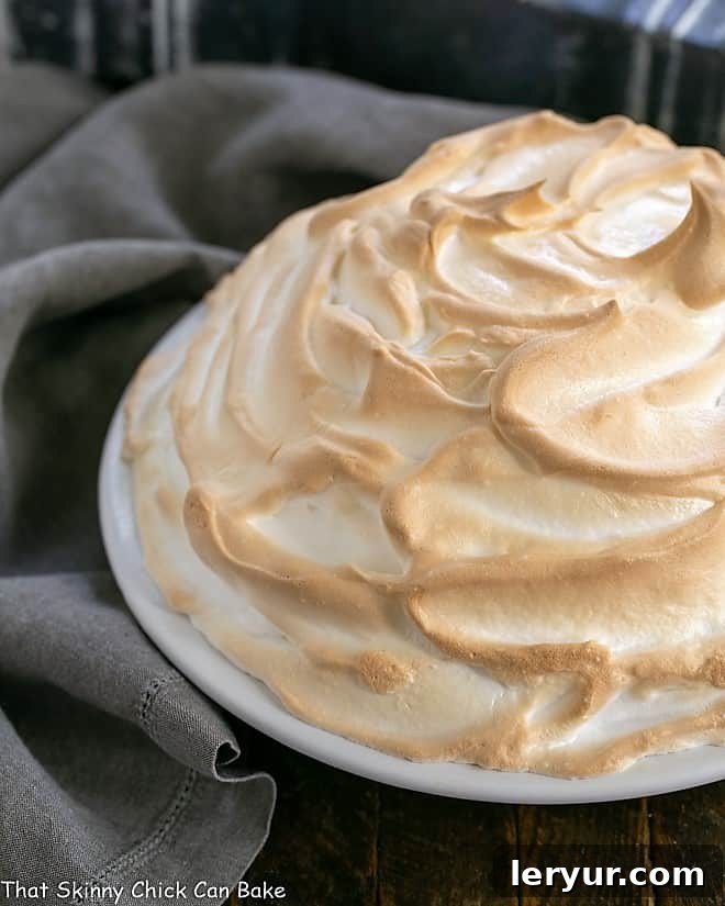 Side view of a perfectly golden-brown toasted meringue on a Brownie Baked Alaska, served in a white pie plate, showcasing its impressive height and delicious layers.