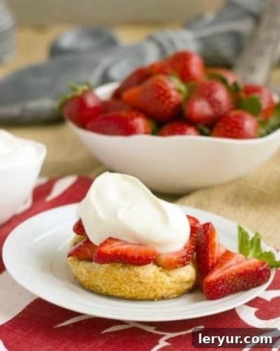 Strawberry Shortcakes with White Chocolate Whipped Cream on a white plate next to a bowl of strawberries, with a spoon digging in.